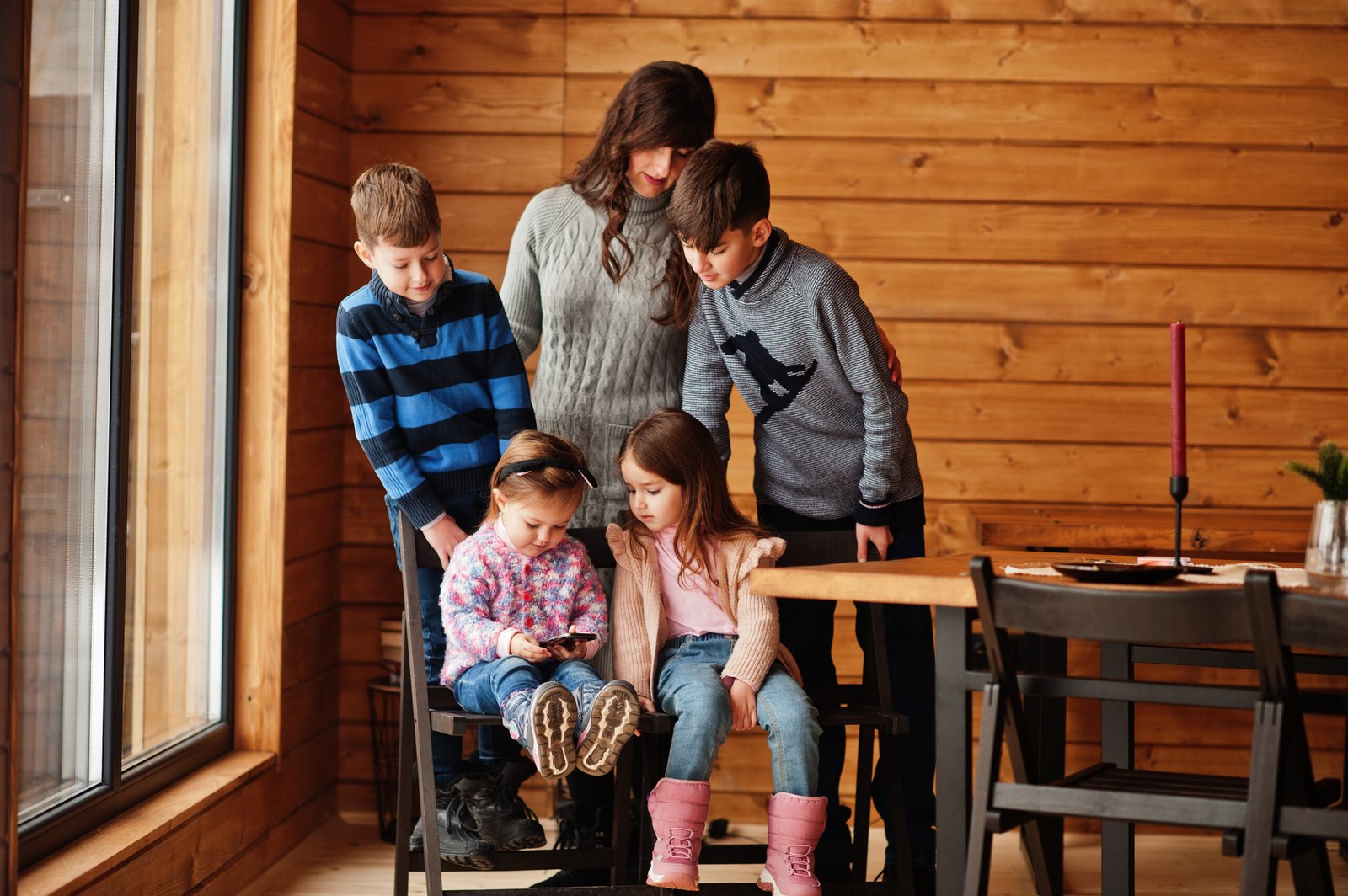 Four kids with mother in modern wooden house watching video in m